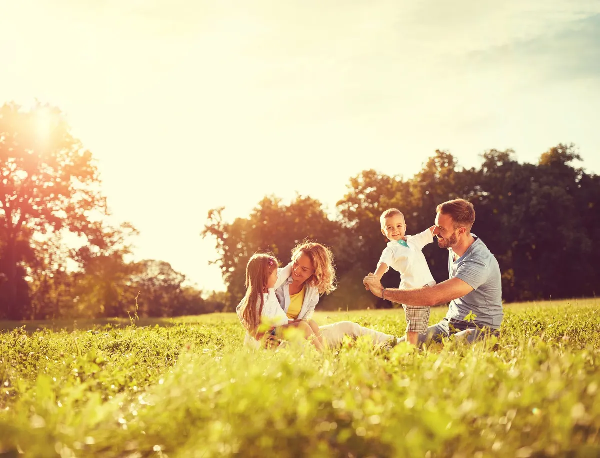 A mother, father, and two children playing together outdoors in a sunlit field
